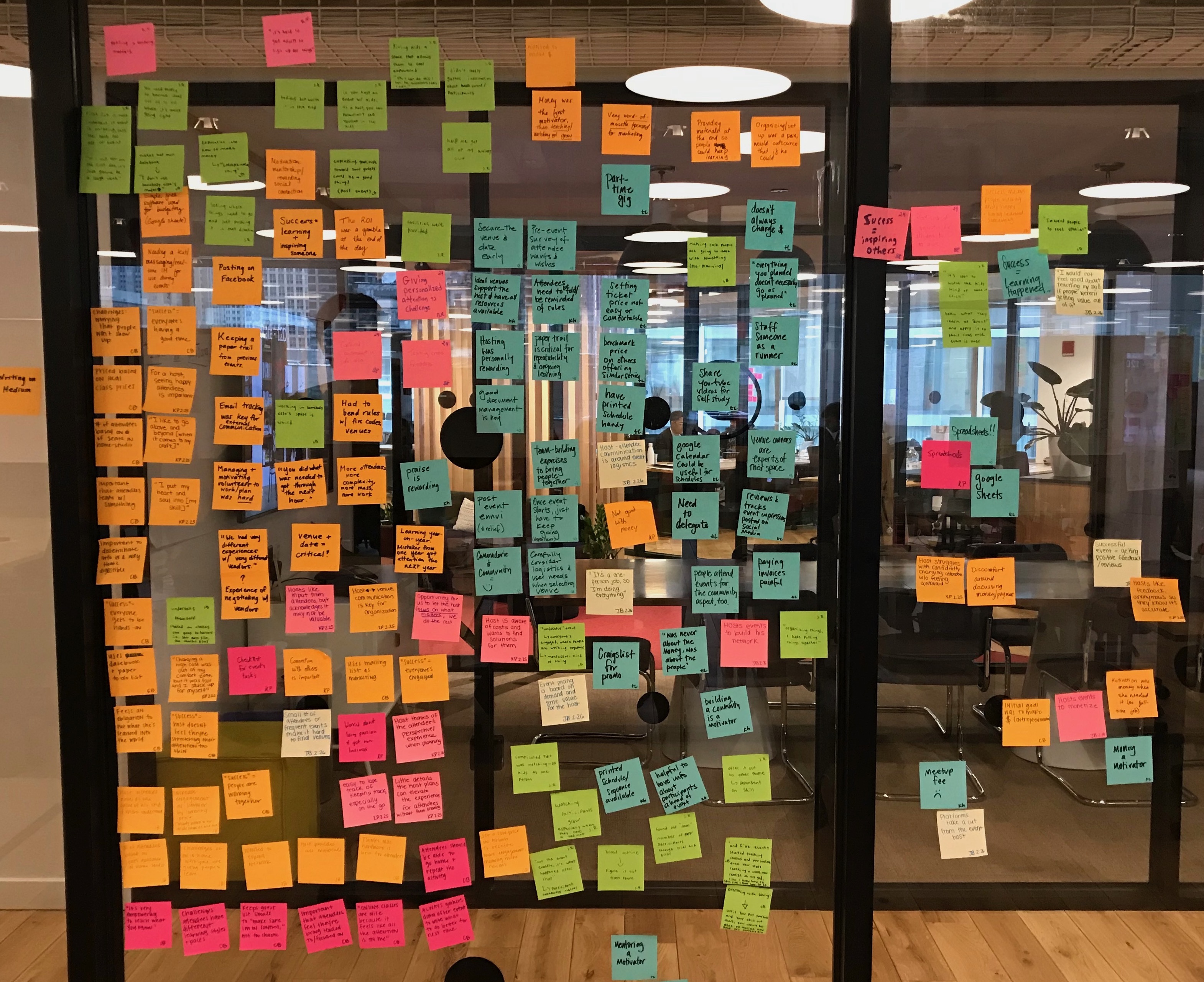 Image of various colored post it notes arranged on a glass wall.
